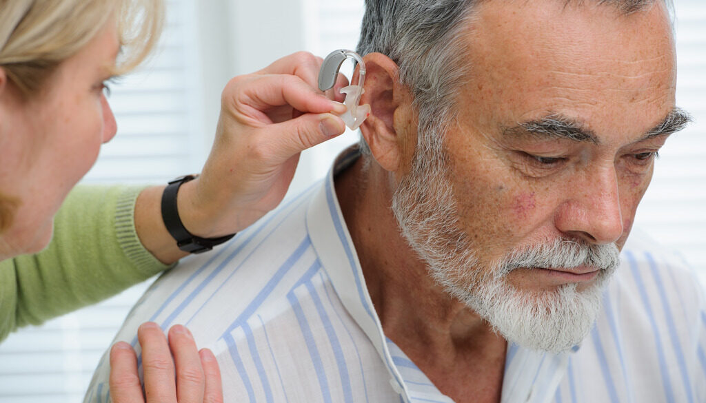 Closeup of a Woman Putting a Hearing Aid Into an Elderly Man's Ear Do Hearing Aids Prevent Dementia