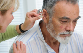 Closeup of a Woman Putting a Hearing Aid Into an Elderly Man's Ear Do Hearing Aids Prevent Dementia