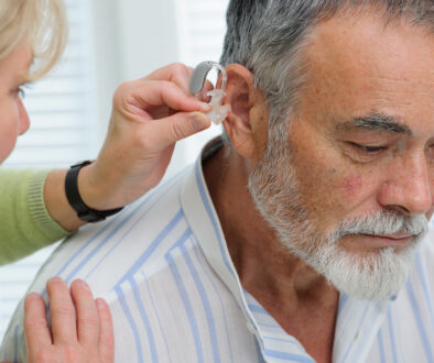 Closeup of a Woman Putting a Hearing Aid Into an Elderly Man's Ear Do Hearing Aids Prevent Dementia