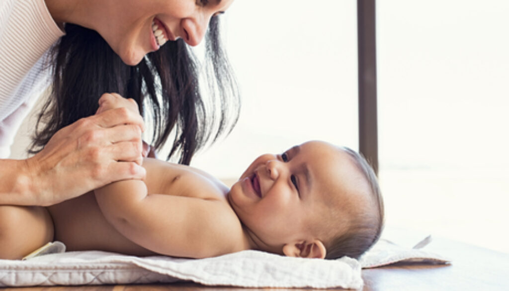 Happy mother playing with baby while changing his diaper. Smilin