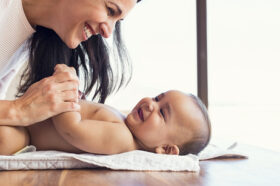 Happy mother playing with baby while changing his diaper. Smilin