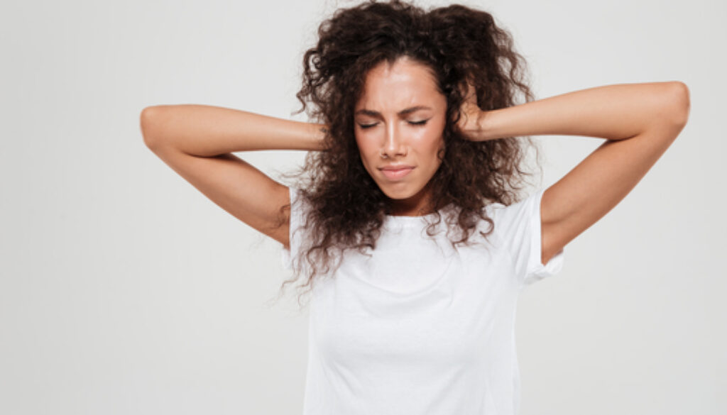 Pretty curly woman covered his ears over gray background