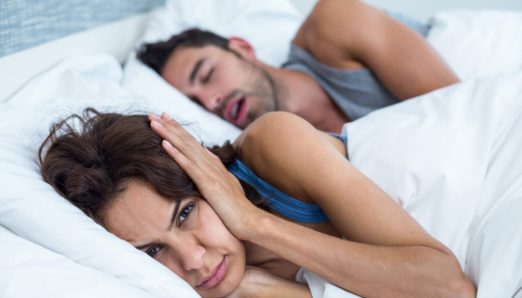 Portrait of woman blocking ears with hands while man snoring on