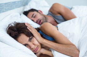 Portrait of woman blocking ears with hands while man snoring on