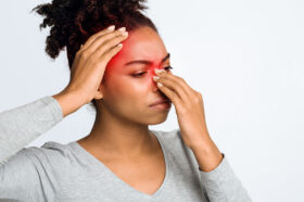 An African American Woman Holding Her Nose and Head That Are Highlighted in Red Can Chronic Sinusitis Affect Your Whole Body